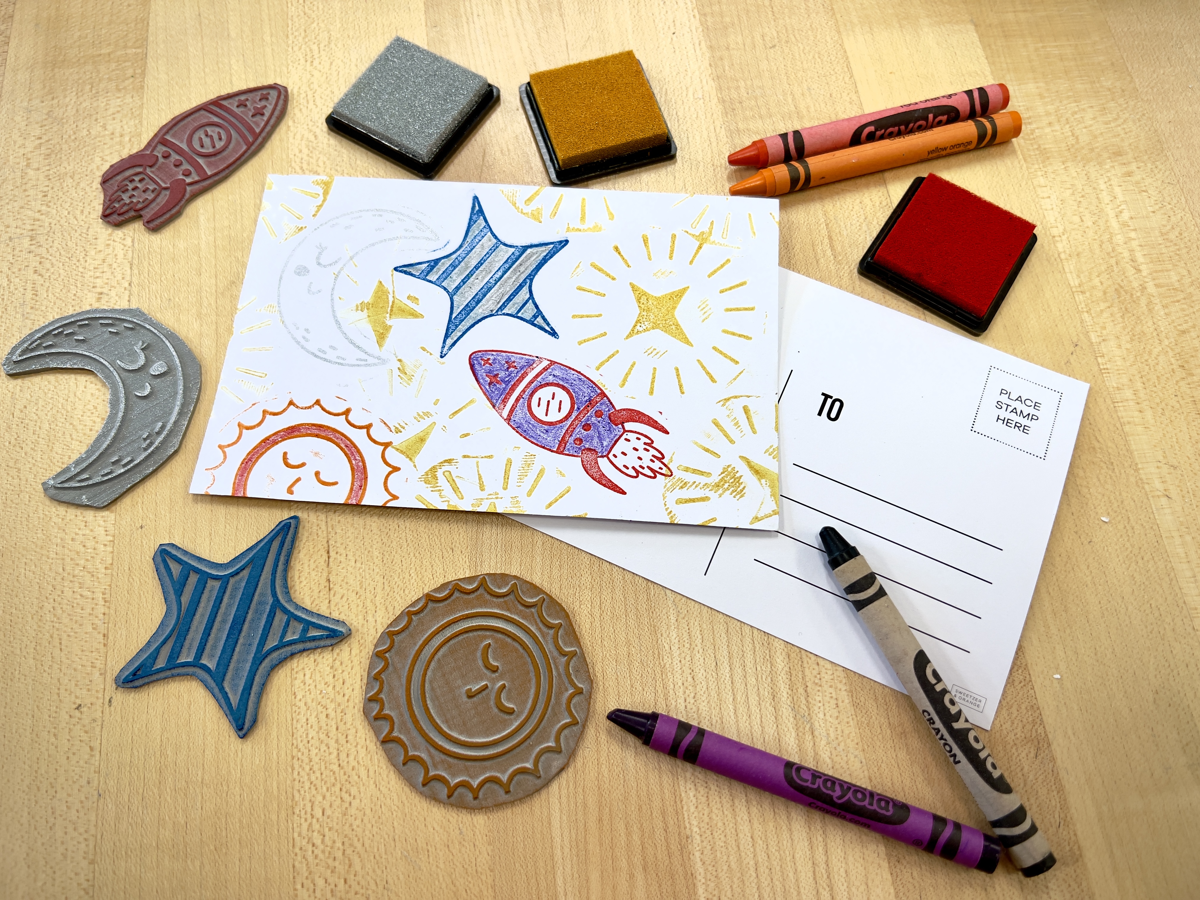 postcards with stamps in shapes of stars, a sun, moon, and rocket ship with different color ink pads and crayons