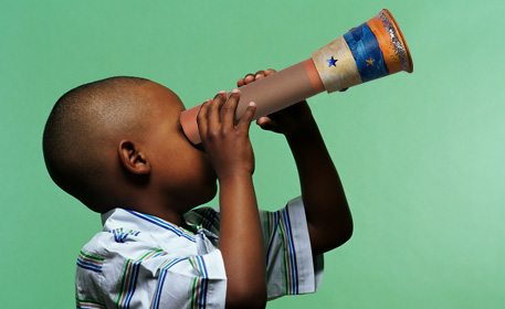 Child holding telescope made of paper towel roll and plastic cup.