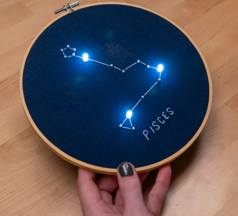 blue material in an embroidery hoop with a Pisces design and LEDs