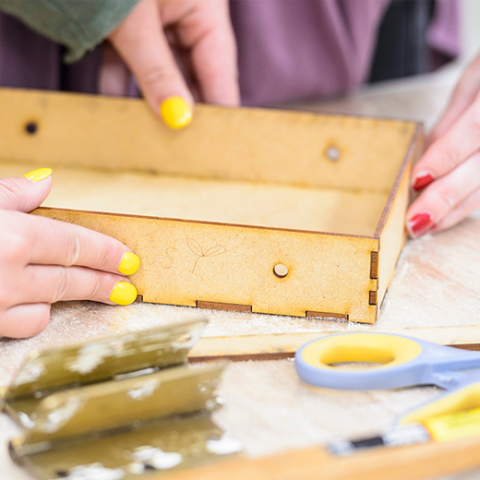 Two pairs of hands putting together a wooden box.