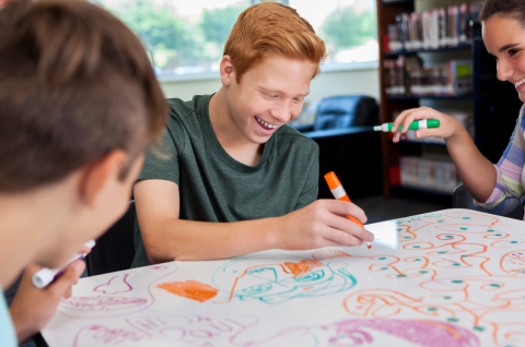 Three teens using markers to draw on whiteboard