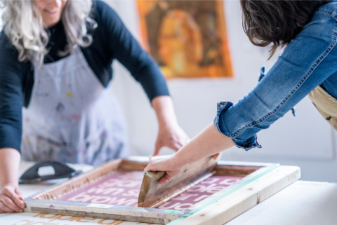 two people working with ink on a screenprinting frame