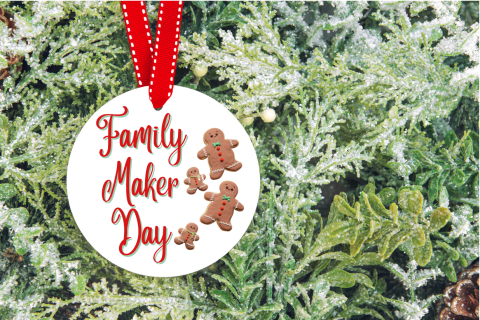 Red ribbon holding round white ornament that says Family Maker Day and has pictures of four gingerbread people on it