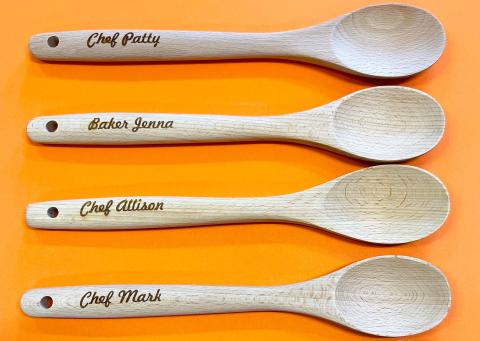 Orange background with four wood spoons that are laser engraved with Chef Patty, Baker Jenna, Chef Allison, and Chef Mark on the handles