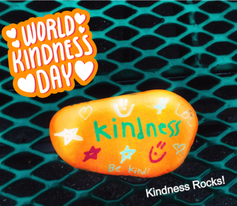 Green grate table with yellow-orange rock that says kindness on it in green with World Kindness Day and Kindness Rocks in text