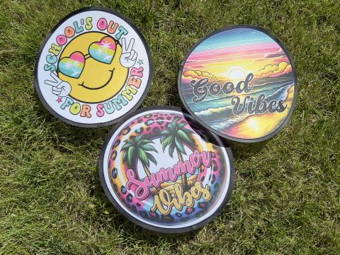 Green grass in the background with three white flexible frisbees with colorful sublimation printing that says Good Vibes and School's Out