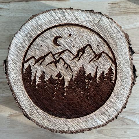 round piece of a tree branch with a picture of trees and mountains laser engraved in a circle
