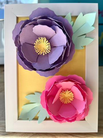 white frame with yellow background and purple flower with green leaves on top and pink flower with green leaves below the purple flower