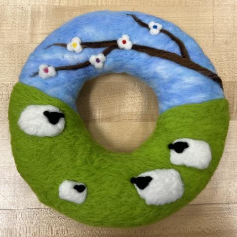 Wool on round shape with 4 different sized sheep on green grass and blue sky with tree branch with 5 white flowers