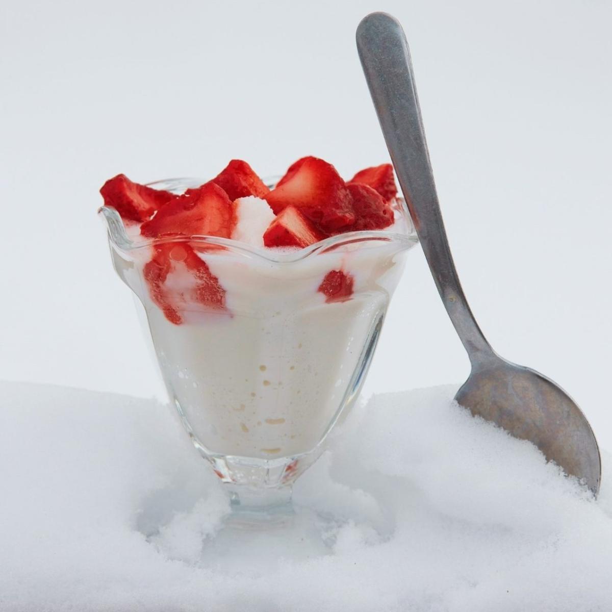 Vanilla ice cream and strawberries in a sundae bowl placed in snow with a metal spoon leaning against it