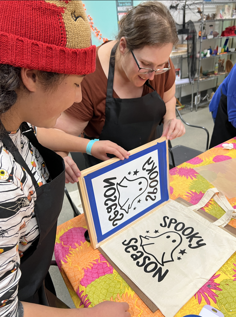 two people screen printing a ghost and words Spooky Season onto a canvas bag