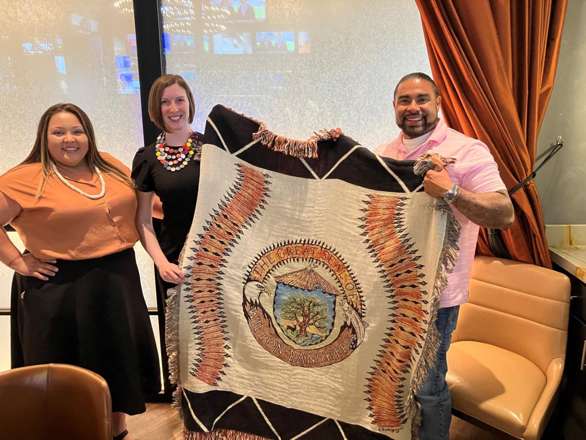 Image of Library Director and tribal representatives holding a ceremonial blanket.