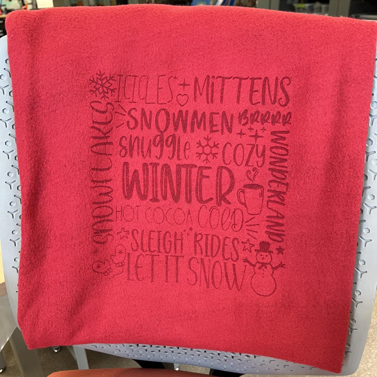 grey chair with red fleece blanket engraved with winter words