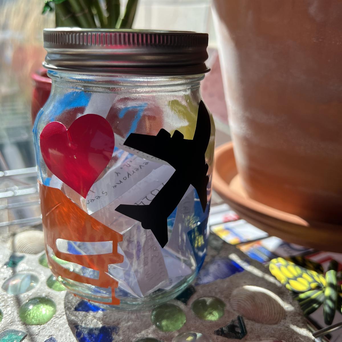 glass mason jar with vinyl decals of a heart, plane, books, with handwritten notes inside the jar